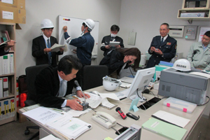 防災センターで無線による指示を発する多谷 司事務部長(自衛消防隊長)と消防署への通報や板書記録を行う自衛消防隊通報連絡班