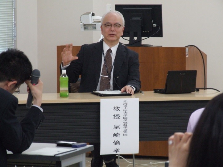 6月25日、保健科学研究院での記者会見で説明する尾崎教授