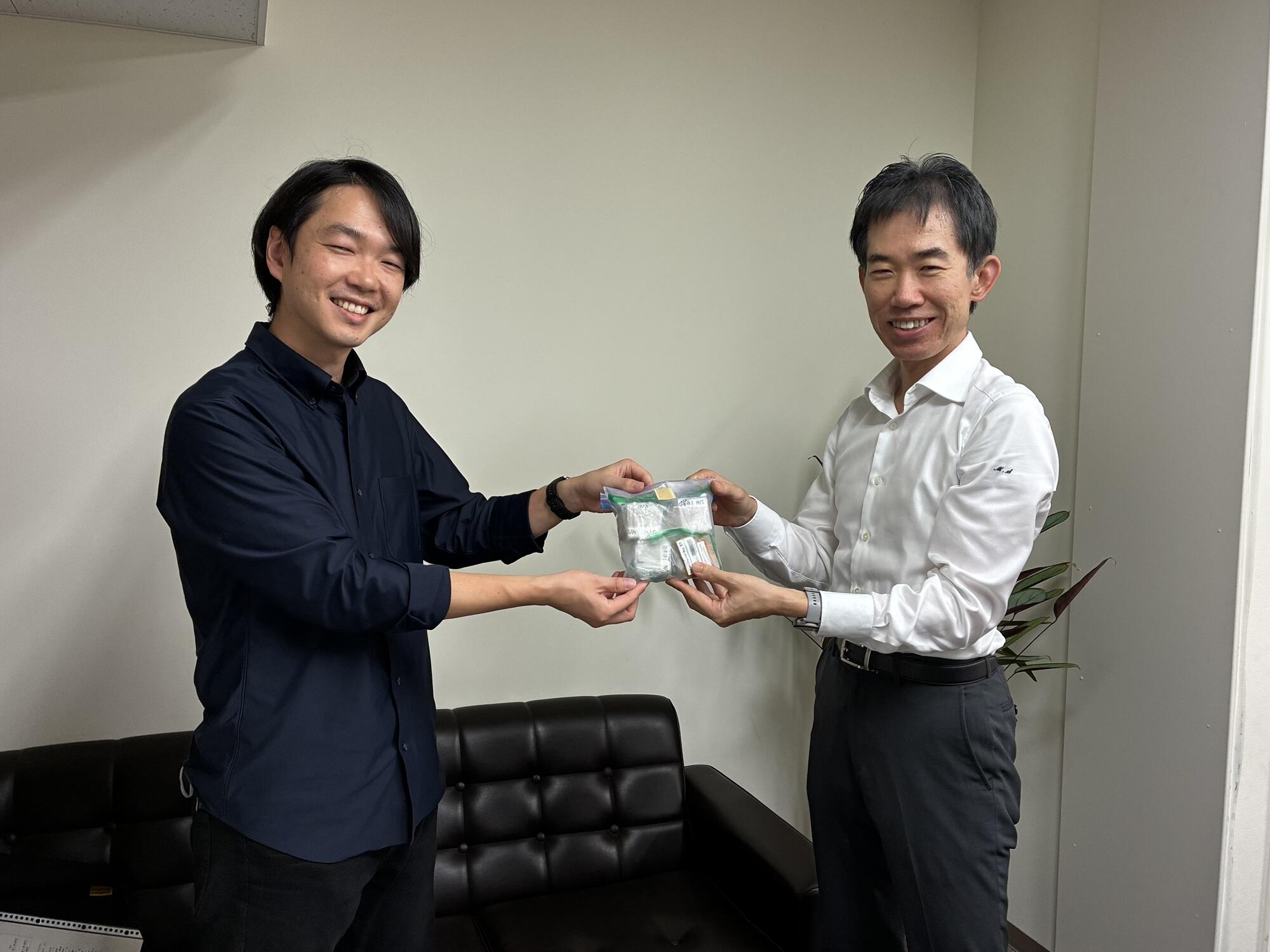 JAXA・桐間氏(左)からショウジョウバエ試料を受け取る園下教授(右)。