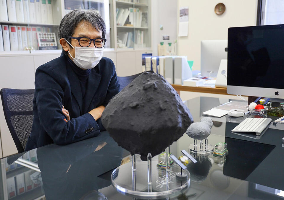 居室にて。小惑星リュウグウの３Dモデル（手前）とイトカワの３Dモデル（奥）とともに。形状はもちろん、大きさの比率や色なども再現されている。リュウグウが黒いのは、有機物を構成する炭素が多く含まれているからと考えられている