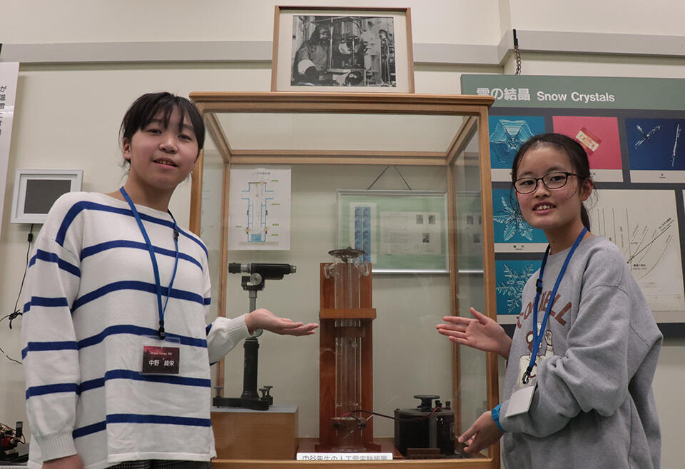 サイエンスレクチャーに参加した中野綺栄さん（小6、左）と中川藍花さん（小6、右）。世界で初めて雪の結晶を人工的に作ることに成功した中谷宇吉郎博士の人工雪生成装置（レプリカ）の前で