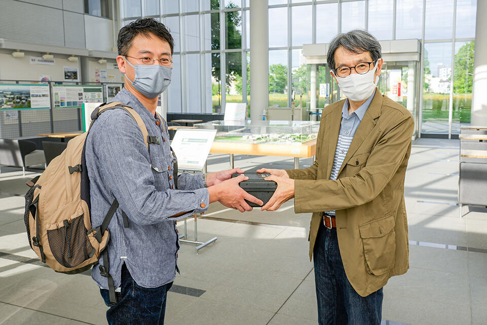 リュウグウサンプルは6月21日、東京大学 理学系研究科 橘省吾教授（左）から北海道大学 理学研究院／創成研究機構の圦本尚義教授（右）に引き渡された