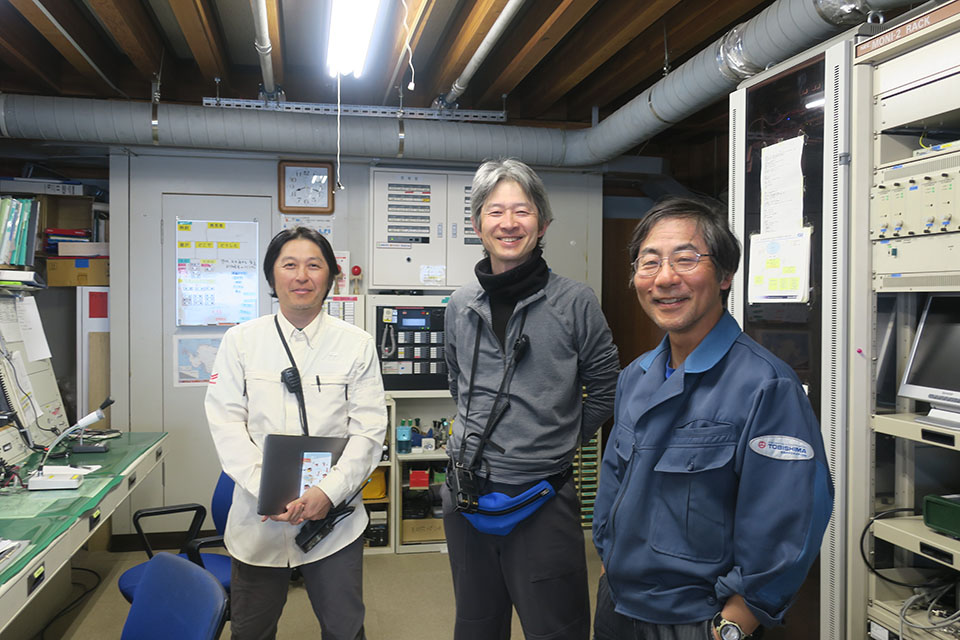 昭和基地の通信室で60・61次越冬隊長らとともに（写真中央が青木 准教授）