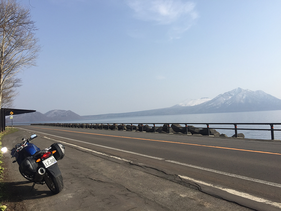 相馬 准教授のバイク、写真右に見えるのは支笏湖（提供：相馬 准教授）